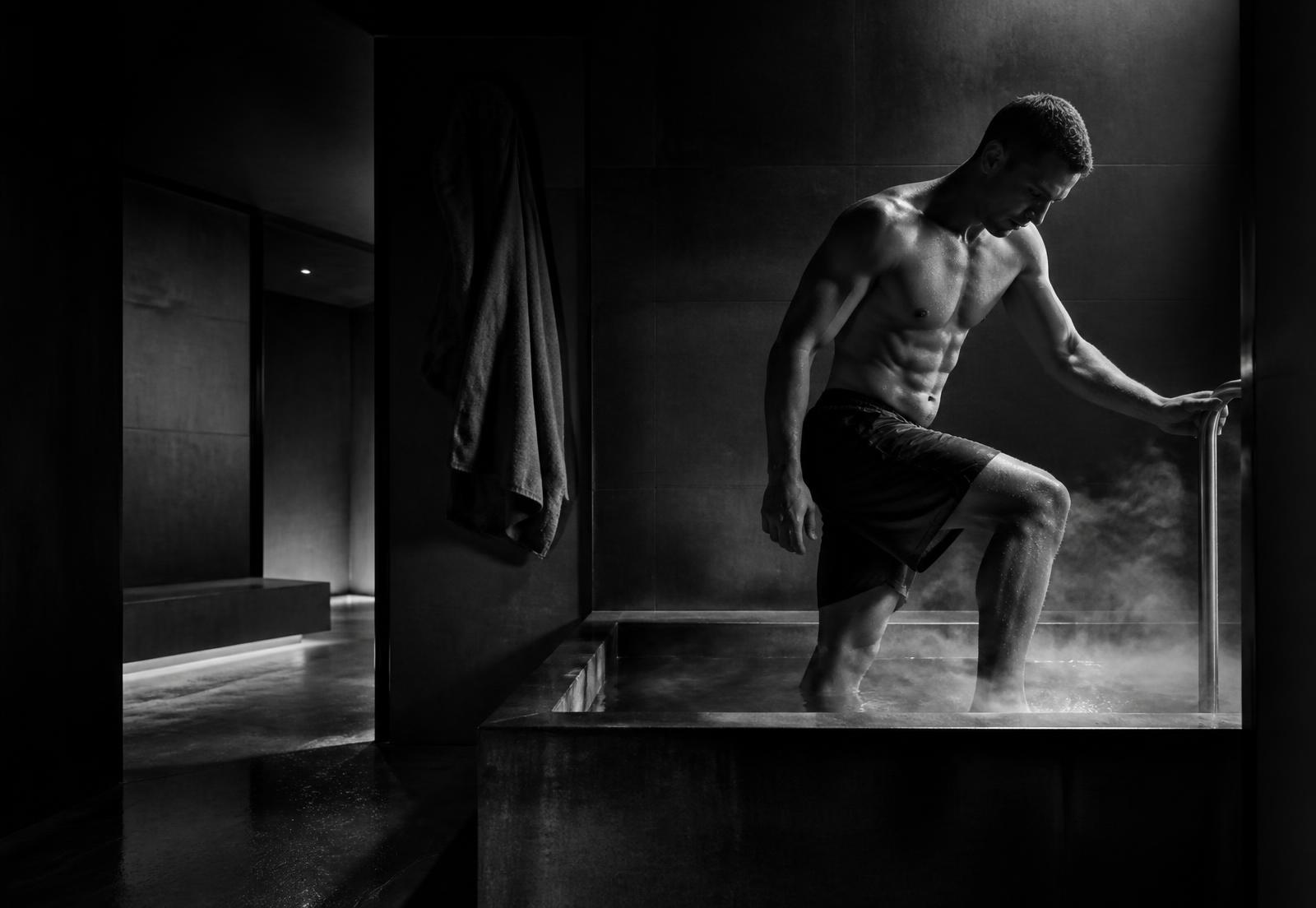 Athlete stepping into a cold plunge in a dark recovery room